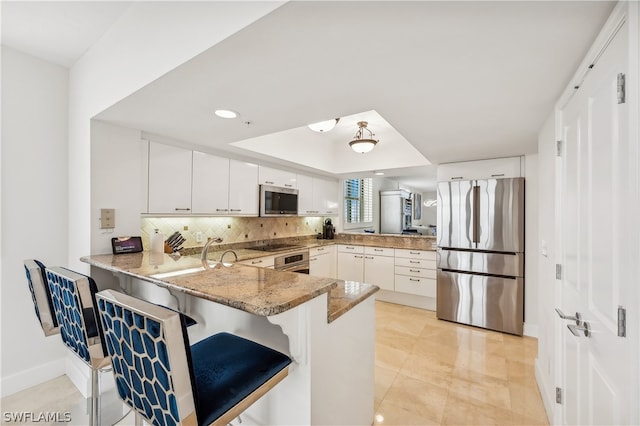 kitchen with white cabinets, stainless steel appliances, kitchen peninsula, and a kitchen bar