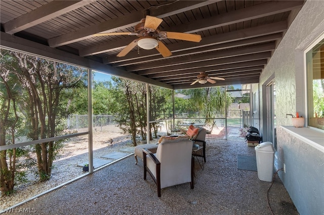 unfurnished sunroom featuring beamed ceiling and ceiling fan