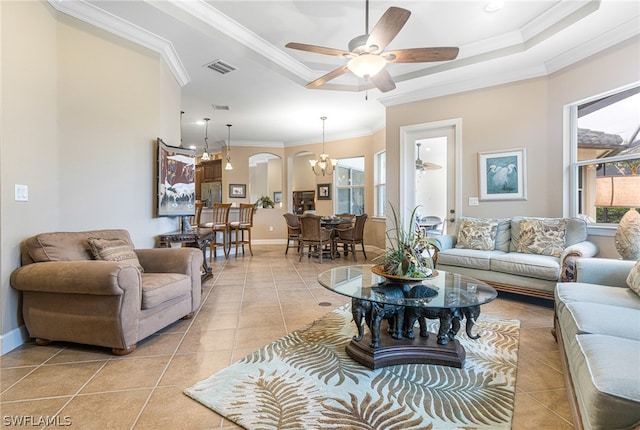 tiled living room with ceiling fan with notable chandelier, a tray ceiling, and crown molding