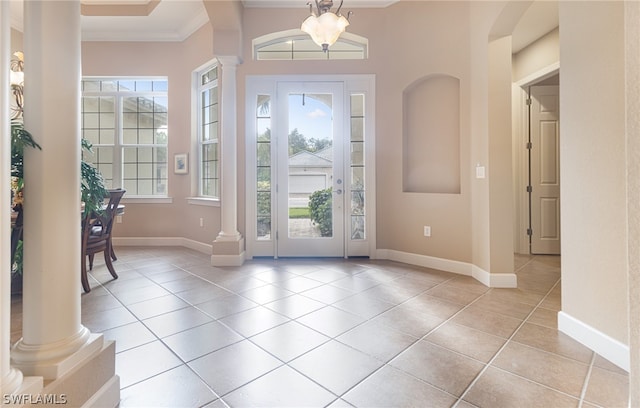 tiled entrance foyer featuring decorative columns, a notable chandelier, and ornamental molding