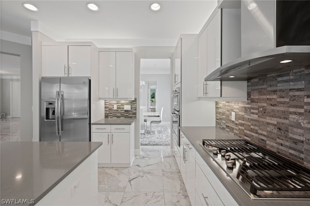 kitchen with backsplash, stainless steel appliances, white cabinetry, and wall chimney exhaust hood