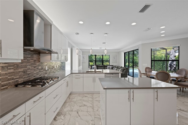 kitchen featuring pendant lighting, wall chimney exhaust hood, a wealth of natural light, and appliances with stainless steel finishes