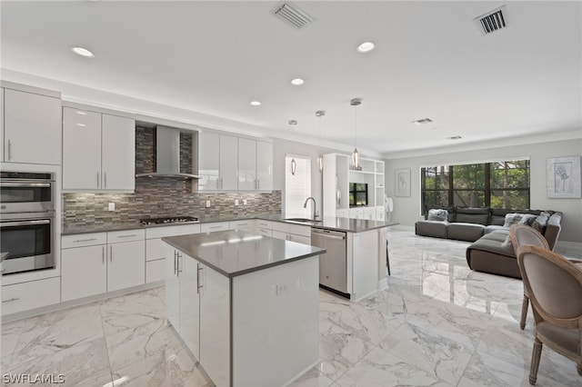 kitchen with sink, wall chimney exhaust hood, decorative light fixtures, a kitchen island, and stainless steel appliances