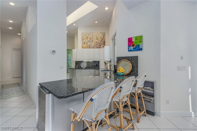 kitchen featuring kitchen peninsula, backsplash, light tile flooring, white cabinetry, and a breakfast bar