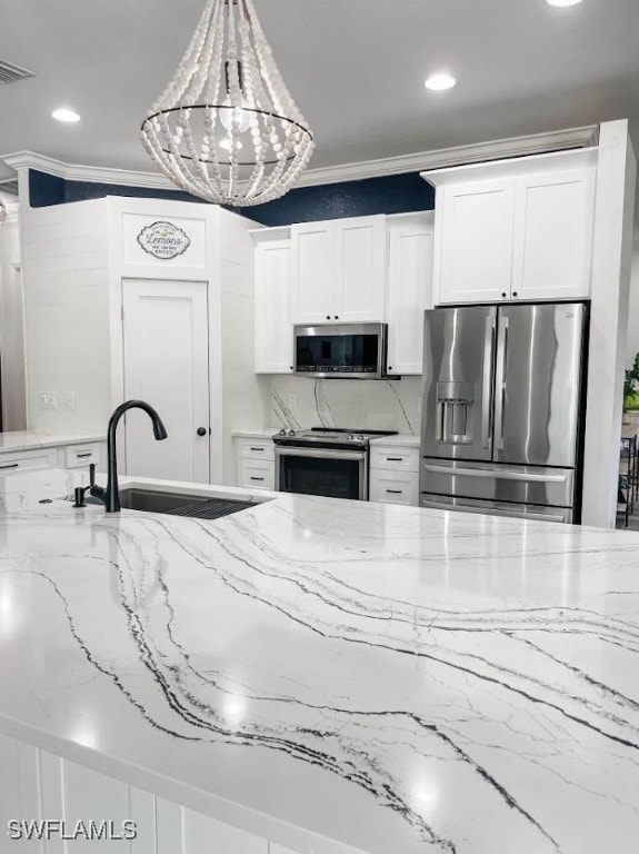 kitchen with stainless steel appliances, decorative light fixtures, white cabinets, ornamental molding, and light stone counters