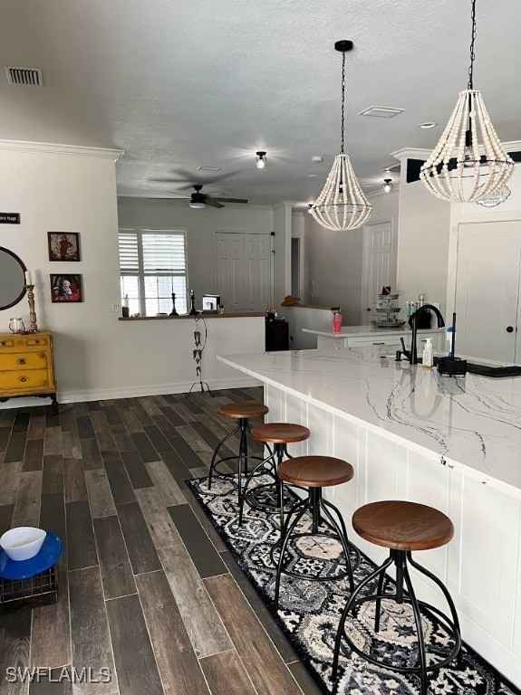 kitchen with light stone counters, ceiling fan, decorative light fixtures, ornamental molding, and dark hardwood / wood-style flooring