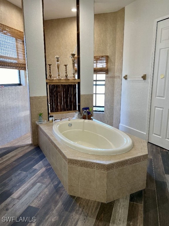 bathroom featuring tiled tub, wood-type flooring, and tile walls