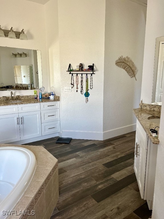 bathroom with wood-type flooring, vanity, and a relaxing tiled tub