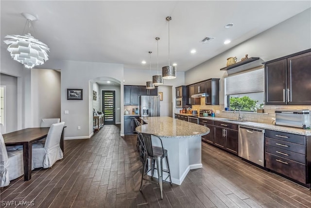 kitchen with pendant lighting, sink, stainless steel appliances, a kitchen island, and decorative backsplash