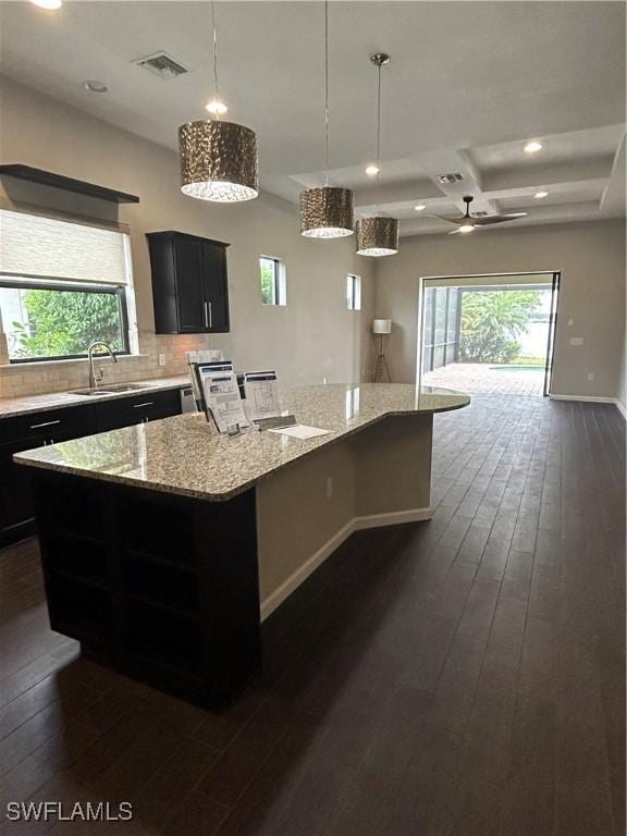 kitchen featuring pendant lighting, sink, light stone counters, a kitchen island, and decorative backsplash