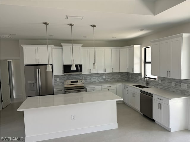 kitchen with appliances with stainless steel finishes, a center island, sink, pendant lighting, and light stone countertops