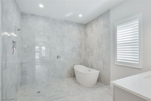 bathroom with tile walls, tile flooring, separate shower and tub, and vanity