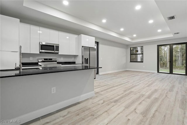 kitchen featuring white cabinets, dark stone countertops, a tray ceiling, light hardwood / wood-style floors, and stainless steel appliances