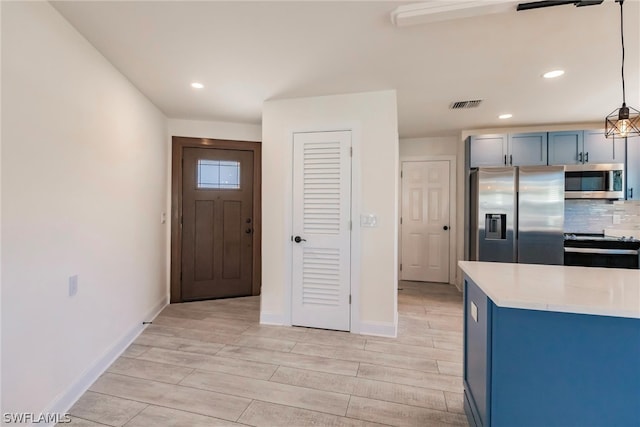 kitchen featuring backsplash, light wood-type flooring, blue cabinetry, decorative light fixtures, and stainless steel appliances