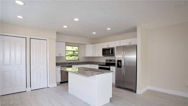 kitchen with white cabinets, stainless steel appliances, stone countertops, sink, and a kitchen island