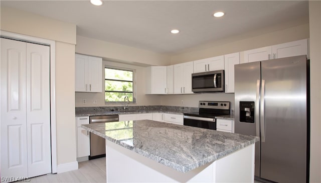 kitchen with a center island, light stone countertops, white cabinetry, stainless steel appliances, and sink