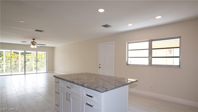 kitchen featuring ceiling fan, white cabinetry, a kitchen island, and light stone countertops