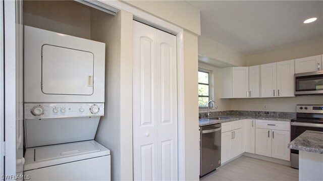 kitchen featuring stacked washer / dryer, white cabinetry, stainless steel appliances, light stone counters, and sink