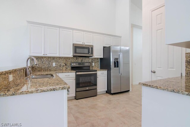 kitchen with light stone countertops, white cabinetry, sink, stainless steel appliances, and a towering ceiling