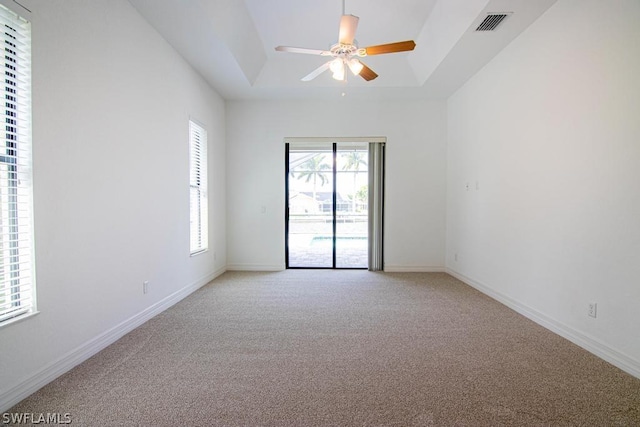 carpeted spare room featuring a raised ceiling and ceiling fan