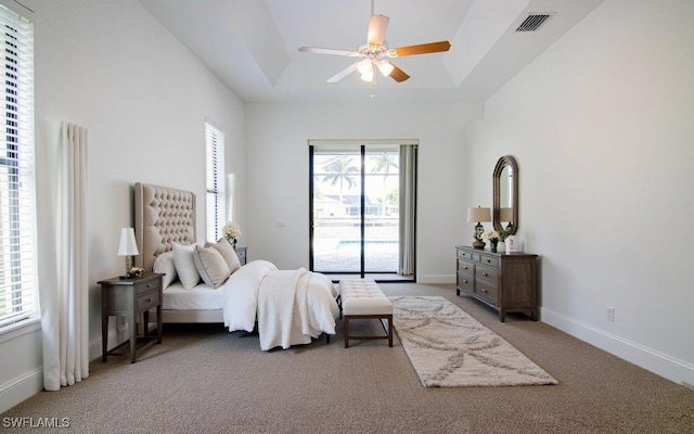 bedroom with a raised ceiling, multiple windows, ceiling fan, and light carpet