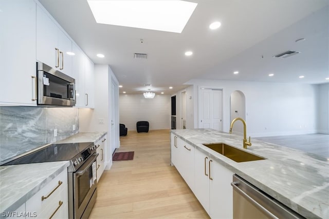 kitchen with light stone counters, white cabinets, sink, light hardwood / wood-style floors, and stainless steel appliances