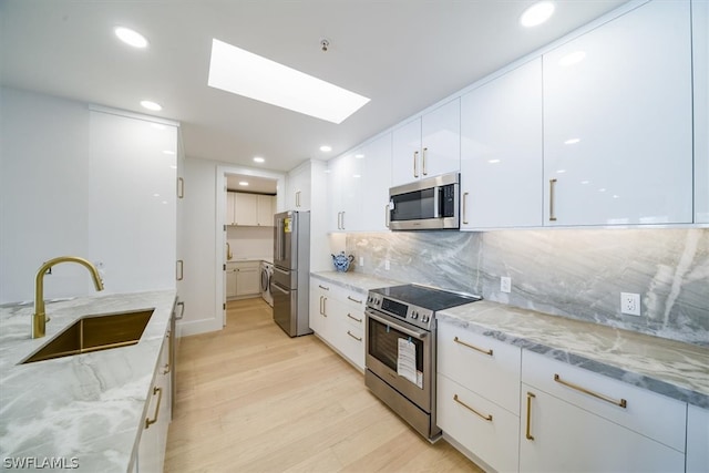 kitchen with sink, backsplash, light wood-type flooring, white cabinetry, and stainless steel appliances