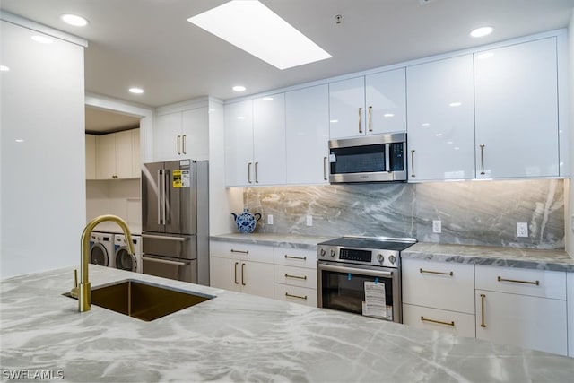 kitchen featuring appliances with stainless steel finishes, sink, tasteful backsplash, washing machine and dryer, and light stone countertops