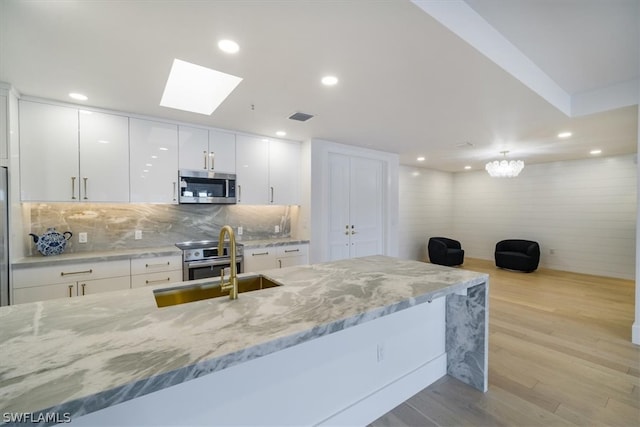 kitchen with light hardwood / wood-style flooring, white cabinets, stove, light stone counters, and a skylight