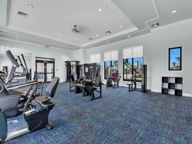 gym with dark carpet, a tray ceiling, ornamental molding, and ceiling fan