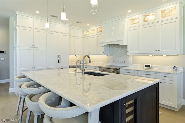 kitchen featuring decorative light fixtures, a center island with sink, white cabinets, sink, and light wood-type flooring