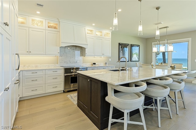 kitchen with sink, a center island with sink, hanging light fixtures, and high end stainless steel range oven