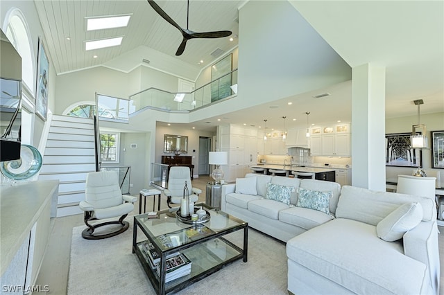 living room featuring a skylight, a towering ceiling, ceiling fan, and light wood-type flooring