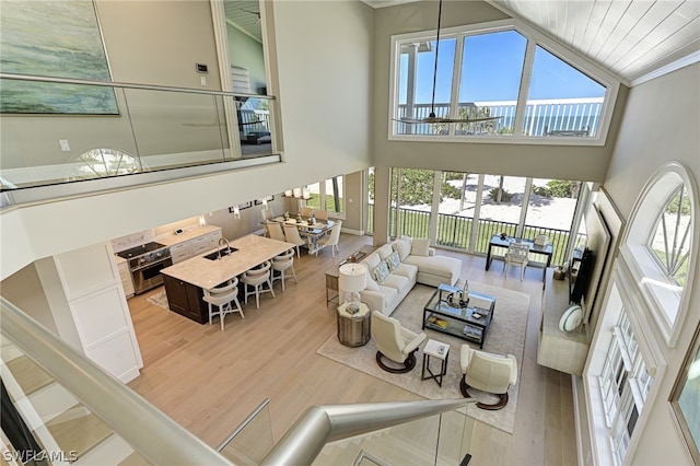 living room featuring plenty of natural light, high vaulted ceiling, crown molding, and light wood-type flooring