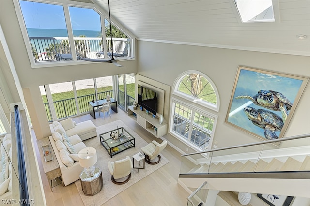 living room with a skylight, a water view, high vaulted ceiling, crown molding, and wood-type flooring