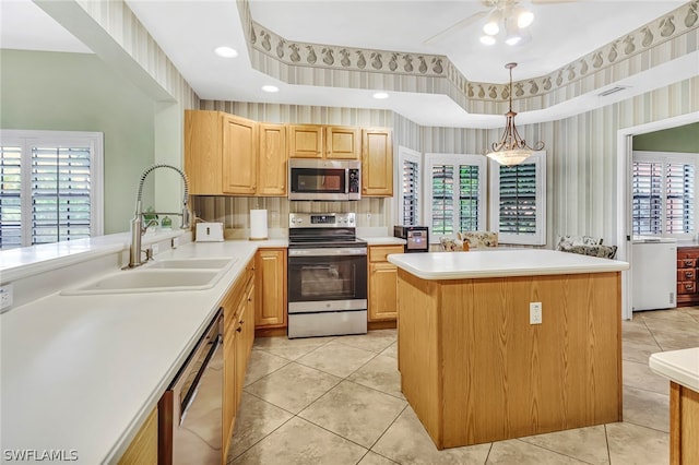 kitchen with appliances with stainless steel finishes, light brown cabinetry, ceiling fan, sink, and a kitchen island