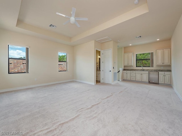 unfurnished living room featuring light carpet, a tray ceiling, and ceiling fan