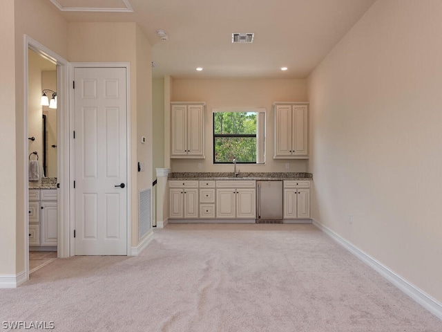 kitchen featuring light stone countertops, dishwasher, sink, cream cabinetry, and light colored carpet