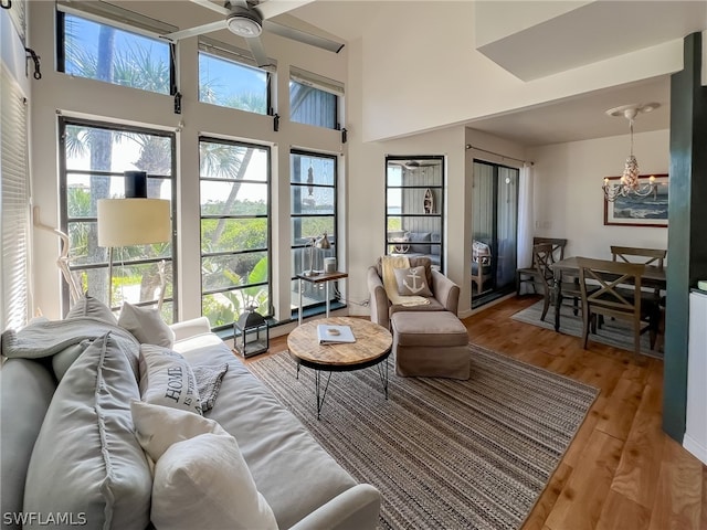 living room with ceiling fan with notable chandelier, hardwood / wood-style floors, and a towering ceiling