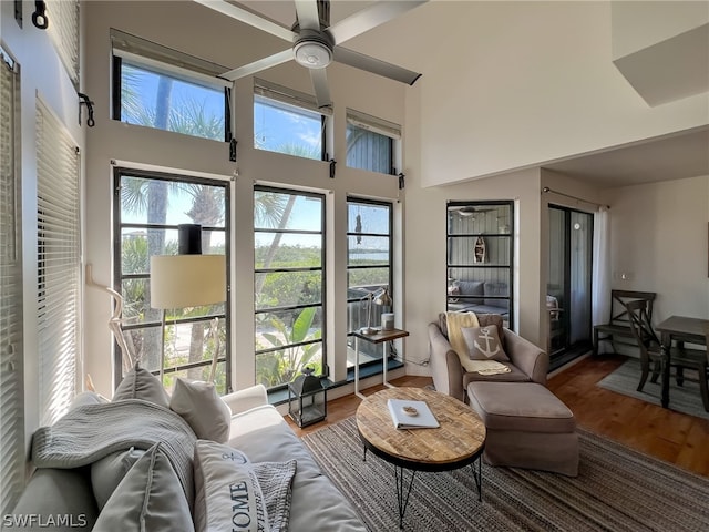 living room with ceiling fan, hardwood / wood-style flooring, and a towering ceiling