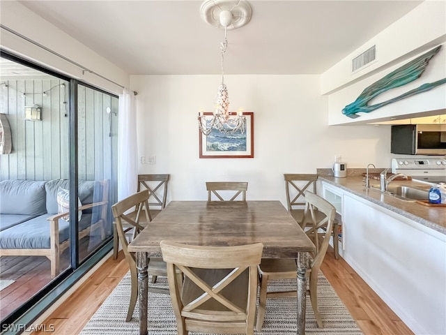 dining room with sink, an inviting chandelier, and light wood-type flooring