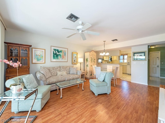 living room featuring ceiling fan with notable chandelier and light hardwood / wood-style flooring