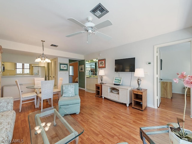 living room with ceiling fan with notable chandelier and light hardwood / wood-style flooring