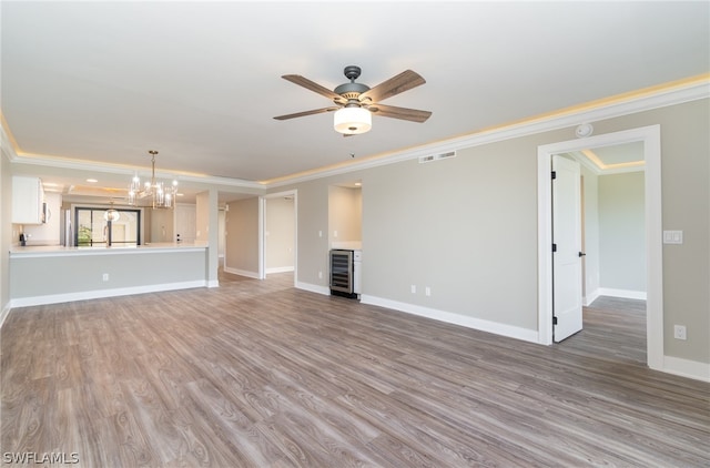 unfurnished living room featuring hardwood / wood-style floors, beverage cooler, ornamental molding, and ceiling fan with notable chandelier