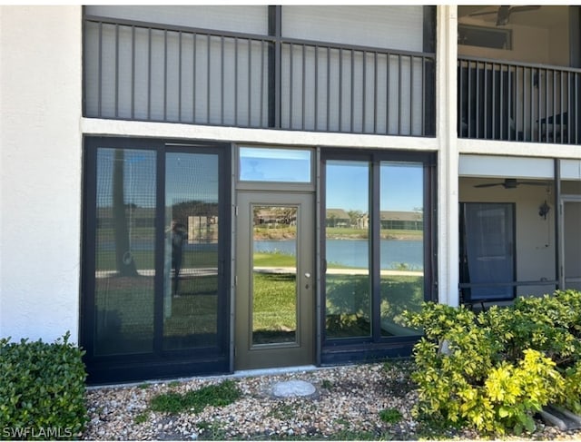 view of exterior entry with a water view, ceiling fan, and a balcony