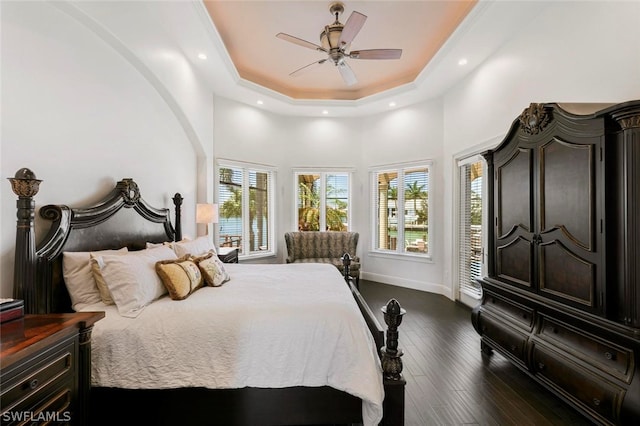 bedroom featuring ceiling fan, access to exterior, a tray ceiling, a high ceiling, and dark hardwood / wood-style floors