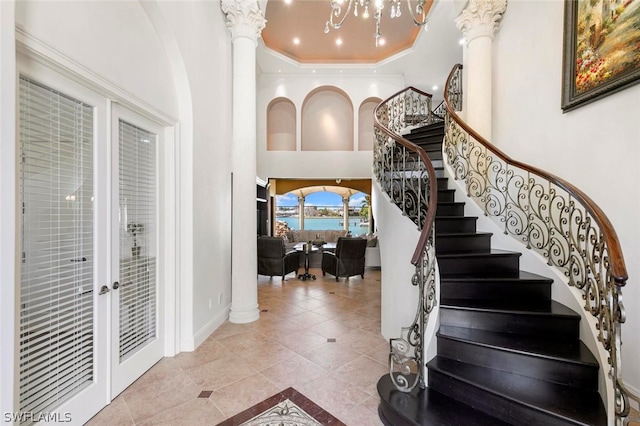 staircase with french doors, tile flooring, a high ceiling, decorative columns, and a chandelier