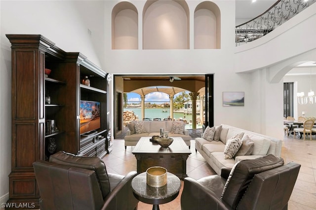 tiled living room with a water view, a towering ceiling, and a notable chandelier