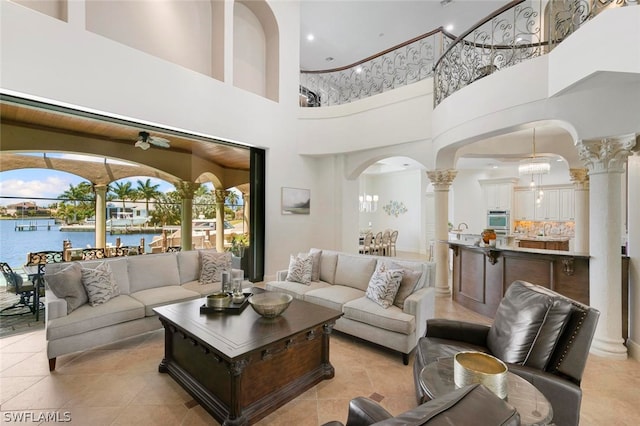 tiled living room with a towering ceiling, decorative columns, and a water view