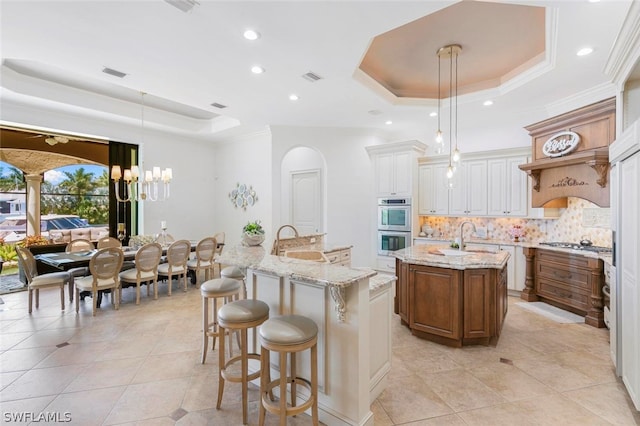 kitchen with a center island with sink, a tray ceiling, white cabinetry, and decorative light fixtures